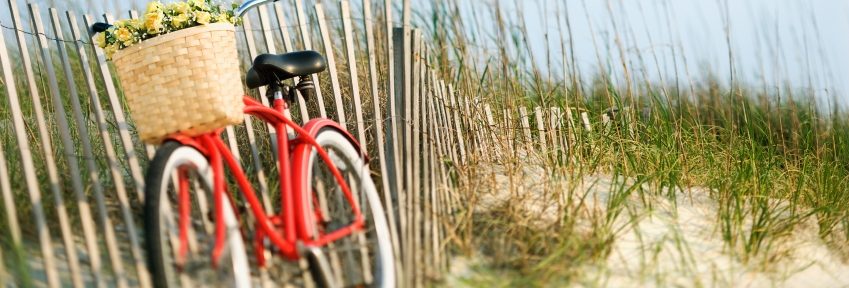 Red vintage bicycle with basket and flowers lleaning against wooden fence at beach.