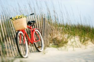 Red vintage bicycle with basket and flowers lleaning against wooden fence at beach.